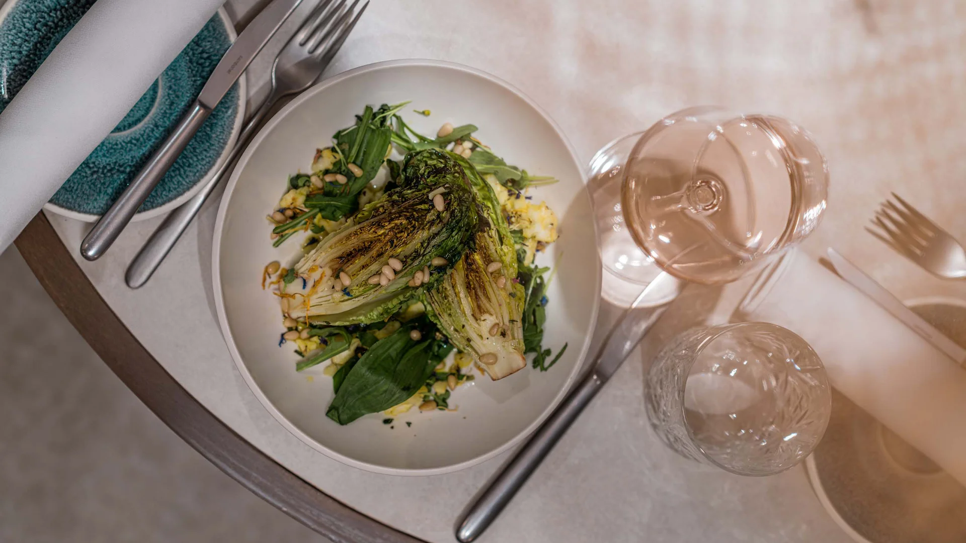 Gegrillter Salat mit Pinienkernen, Besteck und Weinglas auf weißem Tisch